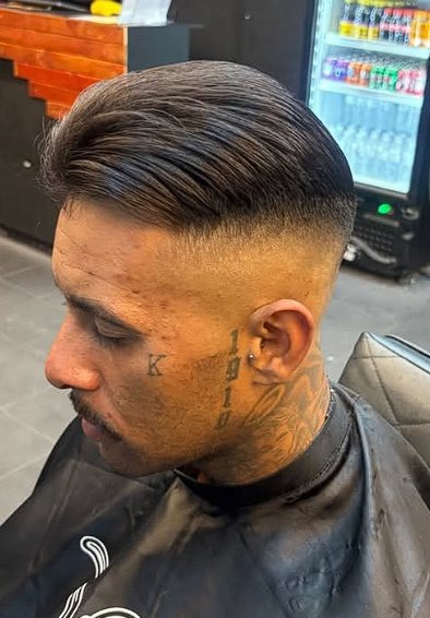 Cliente com degradê alto e cabelo para trás, na cadeira da barbearia